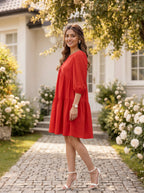 Woman in a red dress standing in a garden with flowers and a house in the background