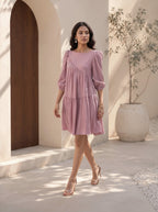 Woman in a pink dress standing in a sunlit outdoor setting with a wooden door and potted plant.