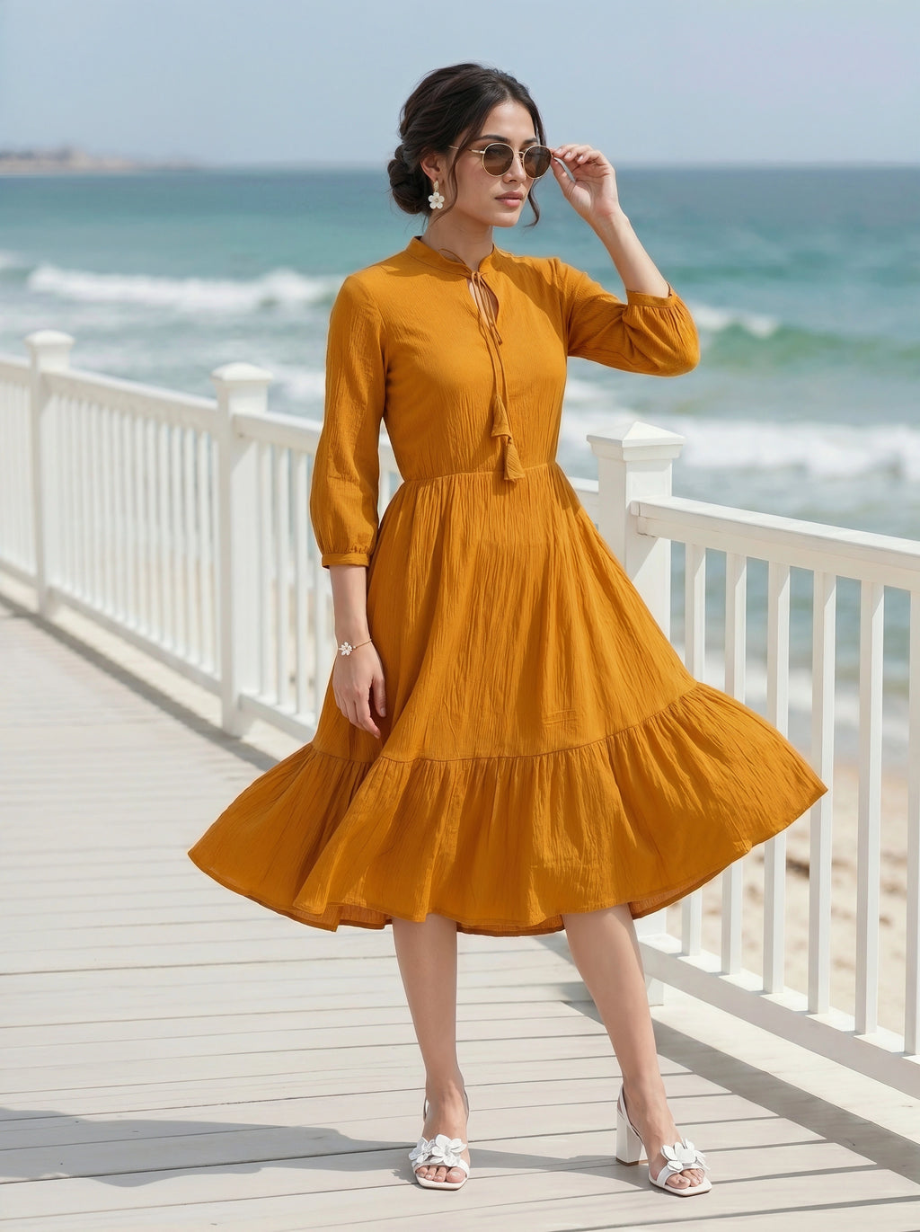 Woman in a mustard yellow dress standing on a wooden deck by the ocean.