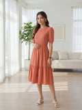 Woman in a coral dress standing in a bright living room.