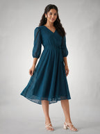 Woman wearing a teal dress with puffed sleeves on a gray background