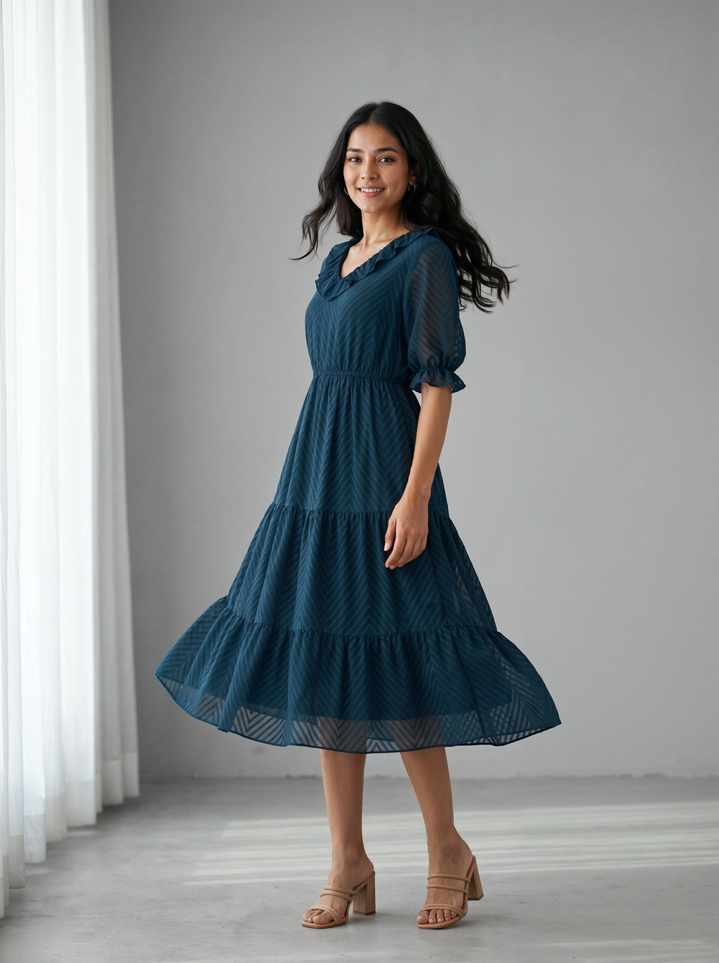 Woman wearing a teal dress standing in a room with white curtains.