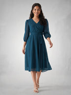 Woman wearing a teal dress on a plain background