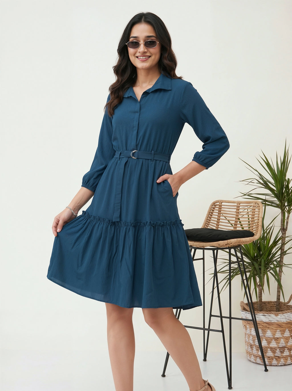 Woman wearing a blue dress with a white background and a plant in the corner