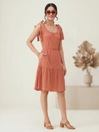 Woman wearing a terracotta dress with ruffled sleeves against a plain background