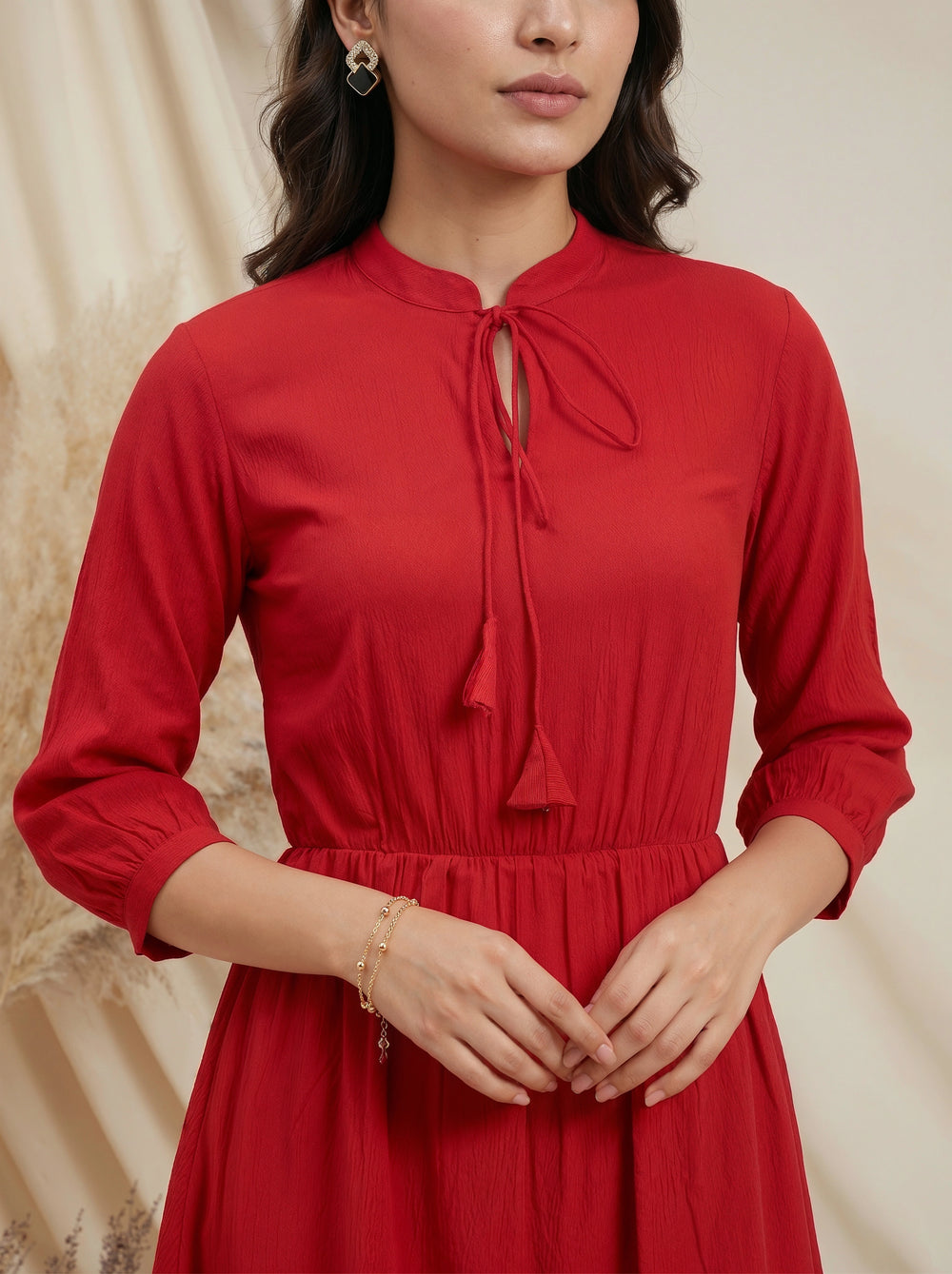 Woman wearing a red dress with a tie neckline against a beige background