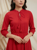 Woman wearing a red dress with a tie neckline against a beige background