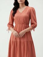 Woman wearing a long rust-colored dress with puffed sleeves on a white background