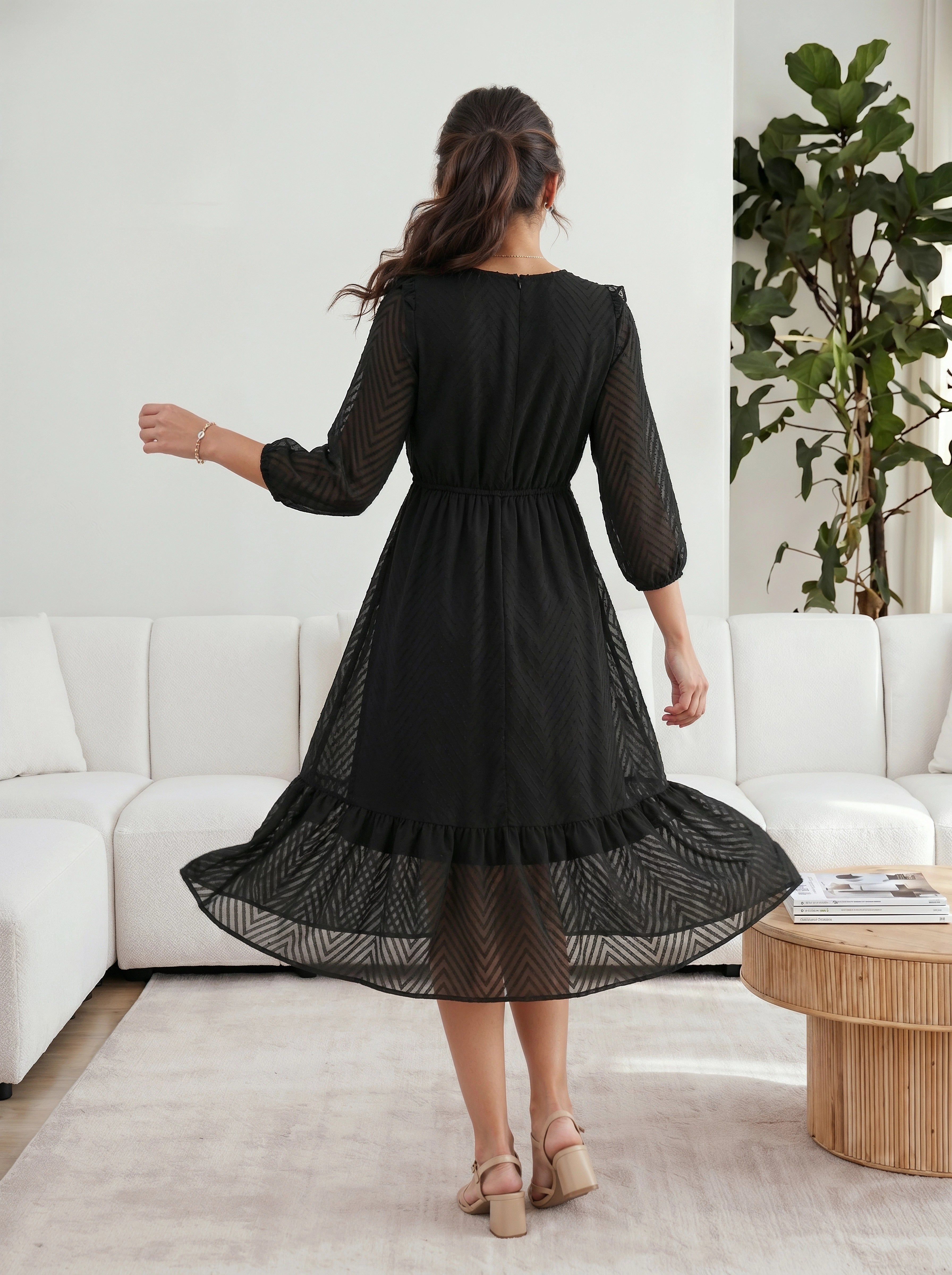 Woman in a black dress standing in a living room with white furniture and a plant.