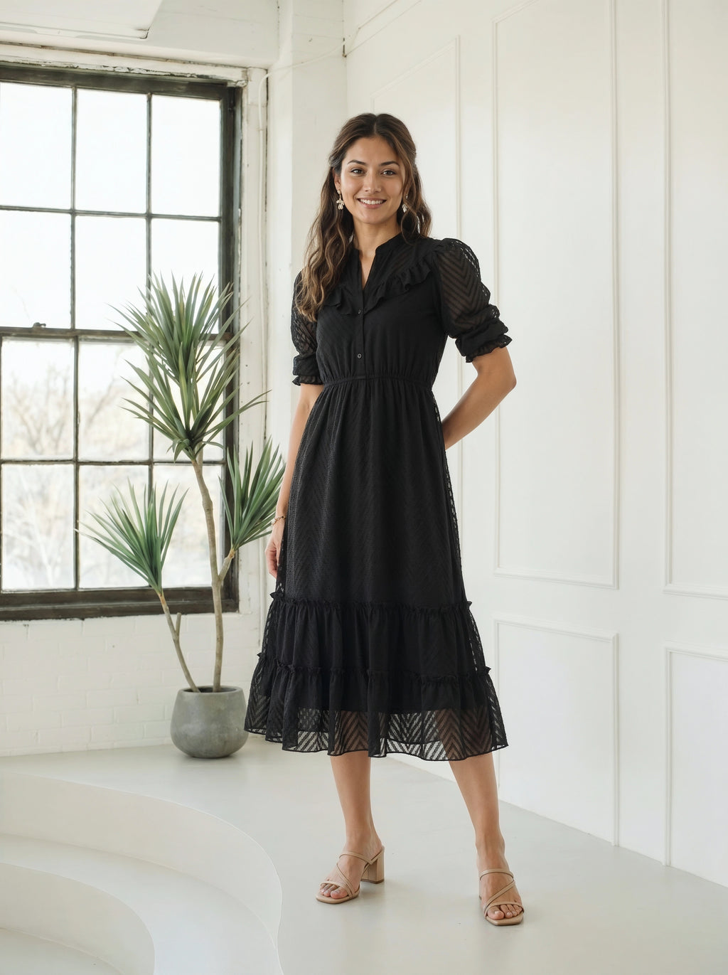 Woman wearing a tiered black dress next to an indoor plant