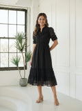 Woman wearing a tiered black dress next to an indoor plant