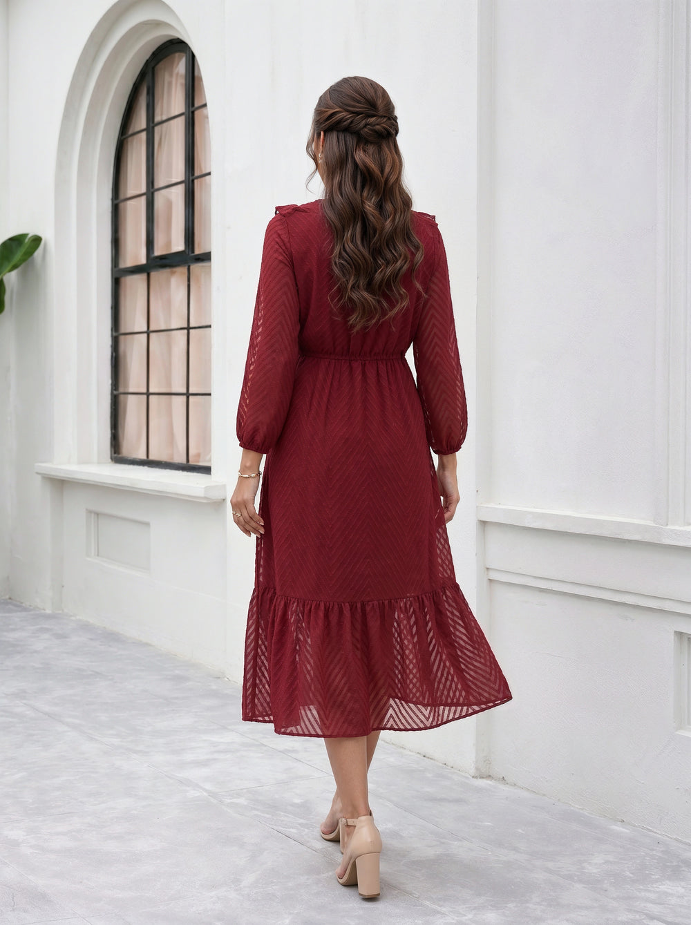 Woman in a red dress standing in a white room with a window.