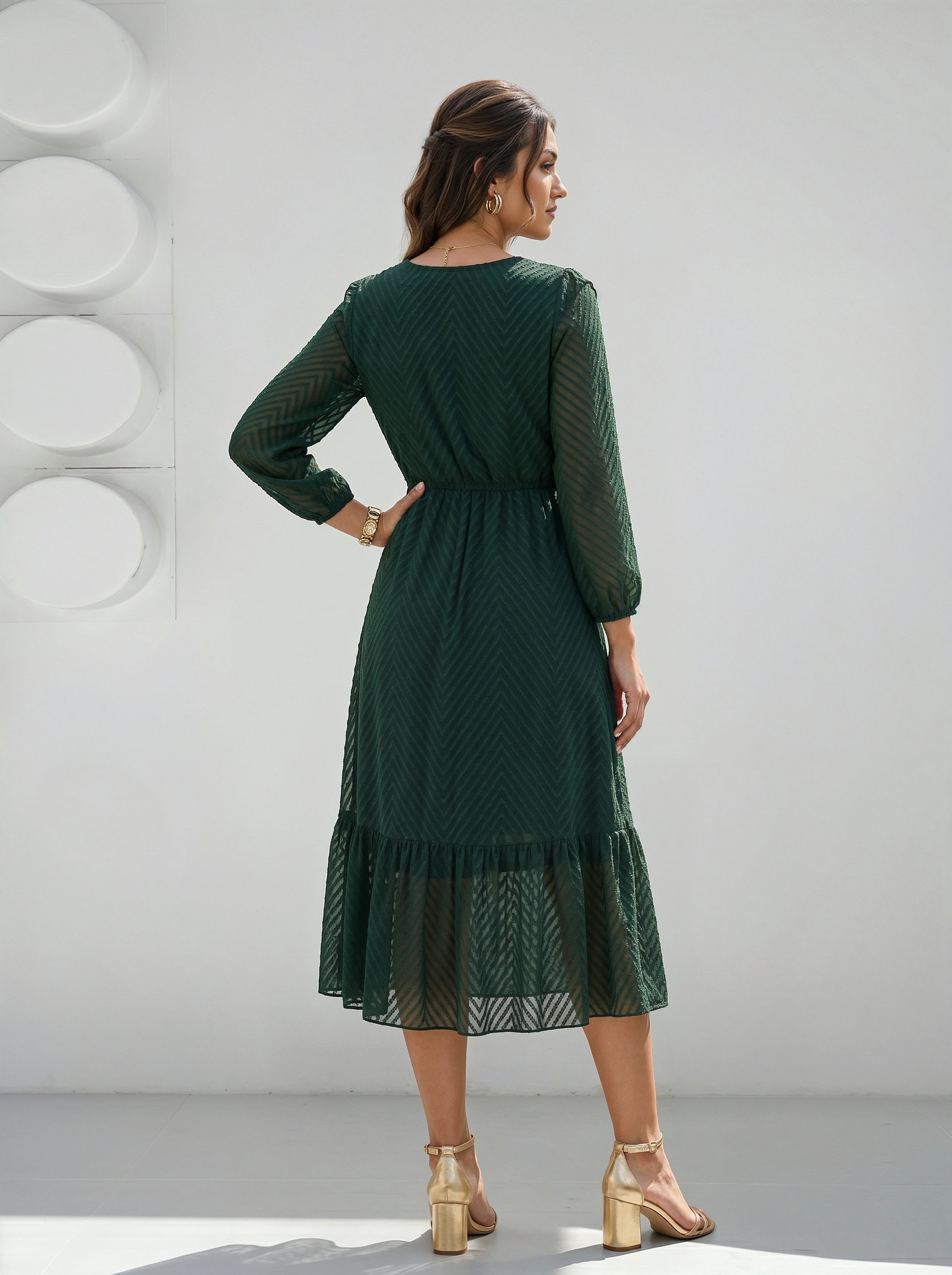 Woman wearing a green dress standing against a white wall.