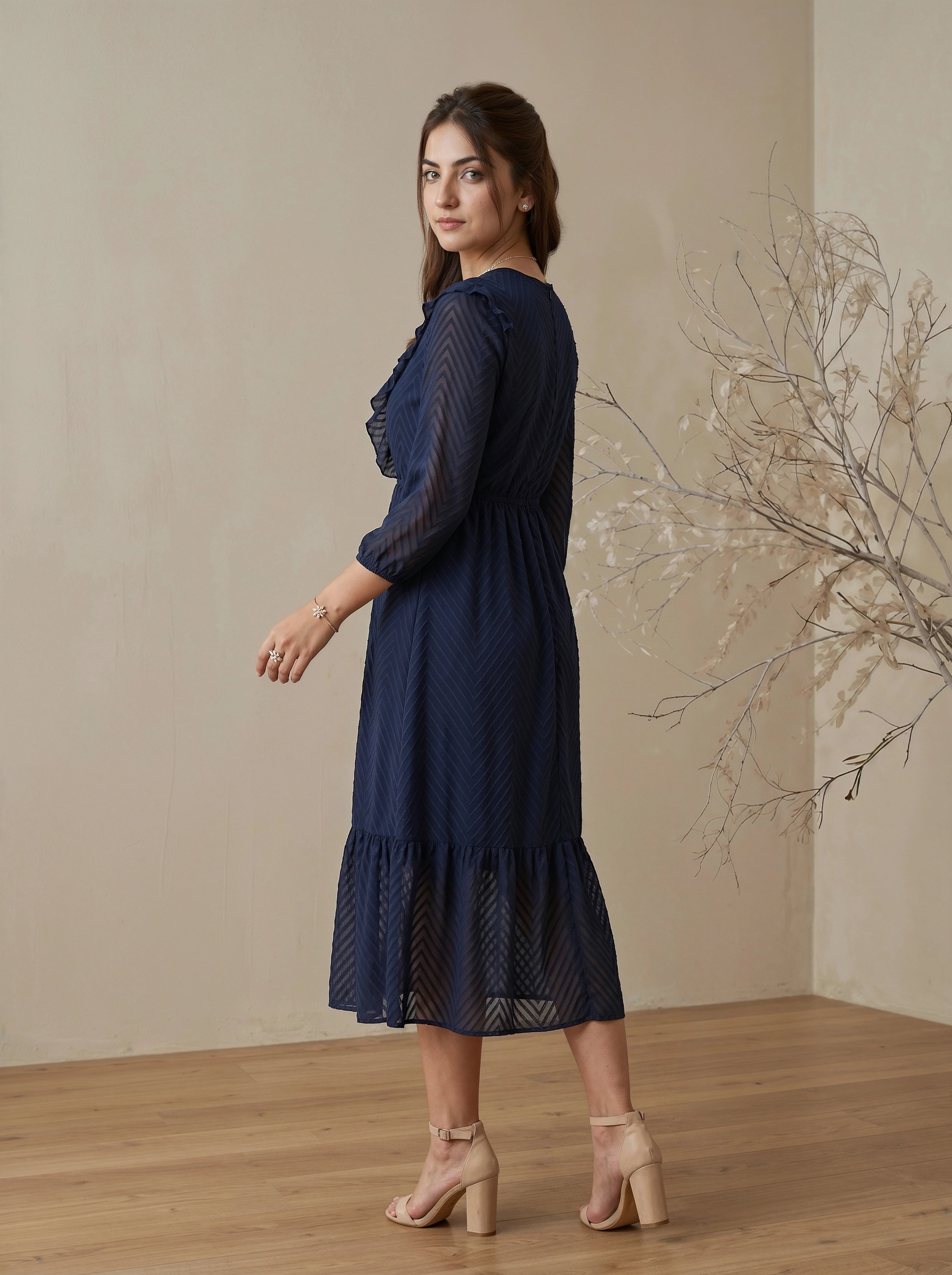 Woman wearing a navy blue dress standing in a room with a beige wall and wooden floor.