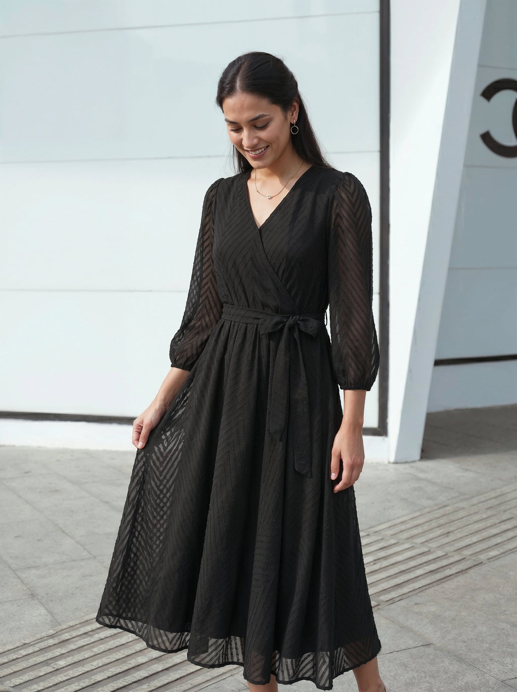 Woman wearing a black dress standing in front of a modern building.