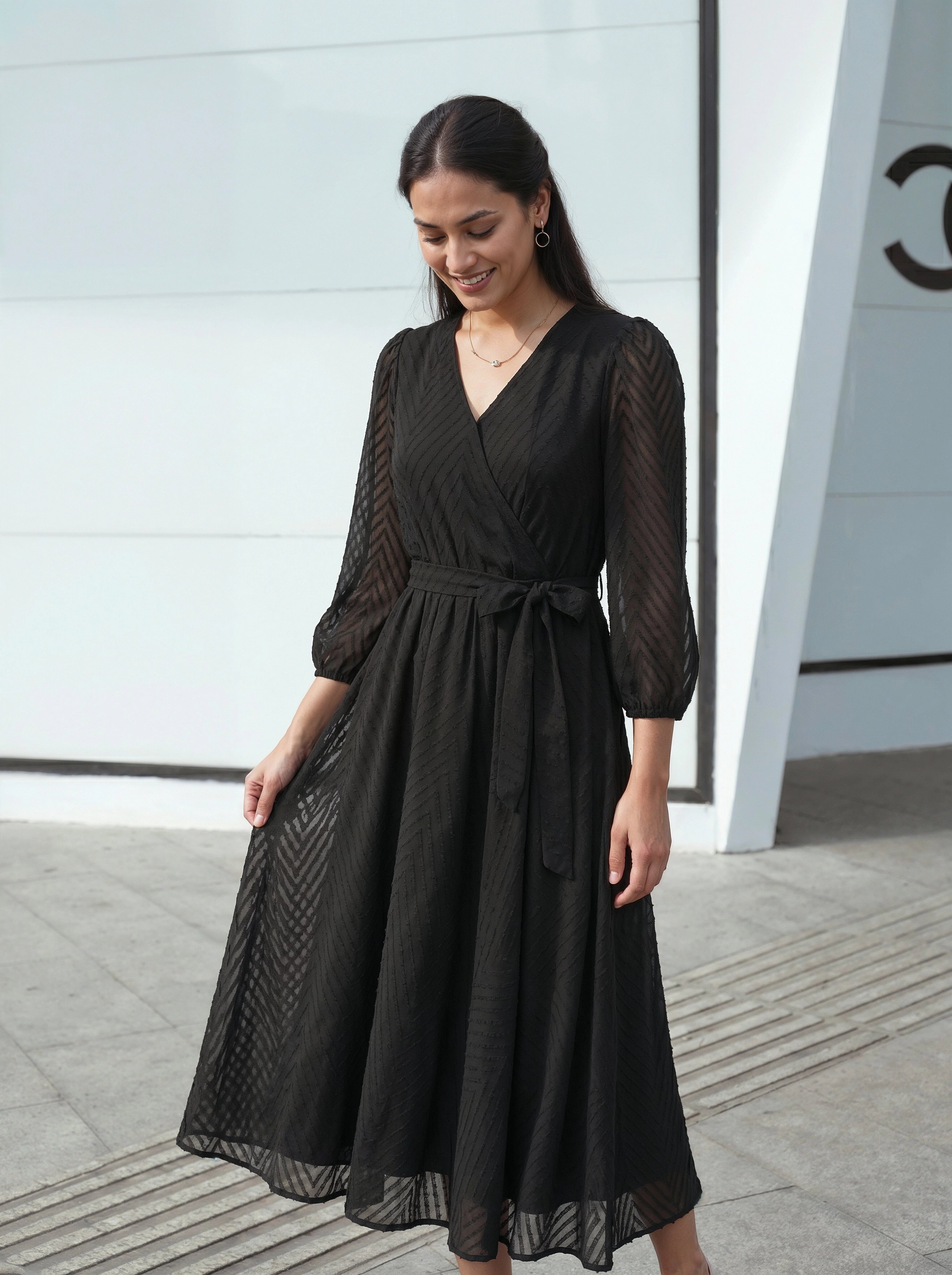 Woman wearing a black dress standing in front of a modern building.