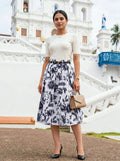 Woman in a floral skirt and white top standing in front of a white architectural structure.