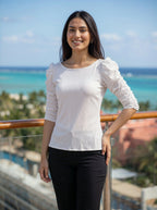 Woman in a white top and black pants standing on a balcony with a scenic background