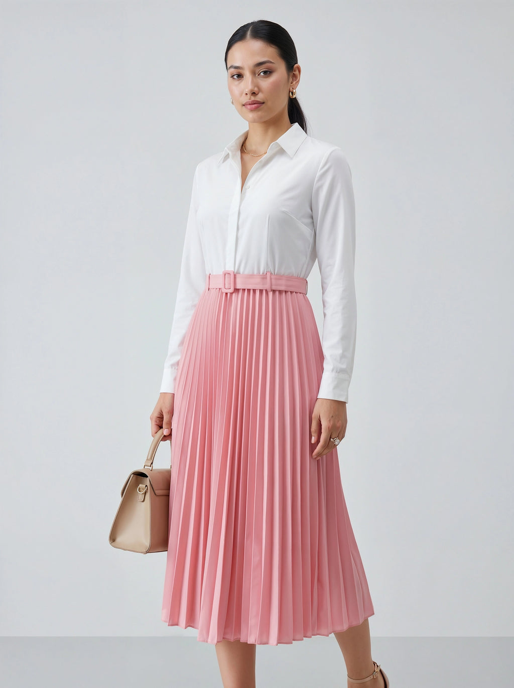 Woman wearing a white shirt and pink pleated skirt holding a beige handbag on a light gray background
