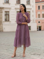 Woman in a purple dress standing on a cobblestone street with buildings in the background