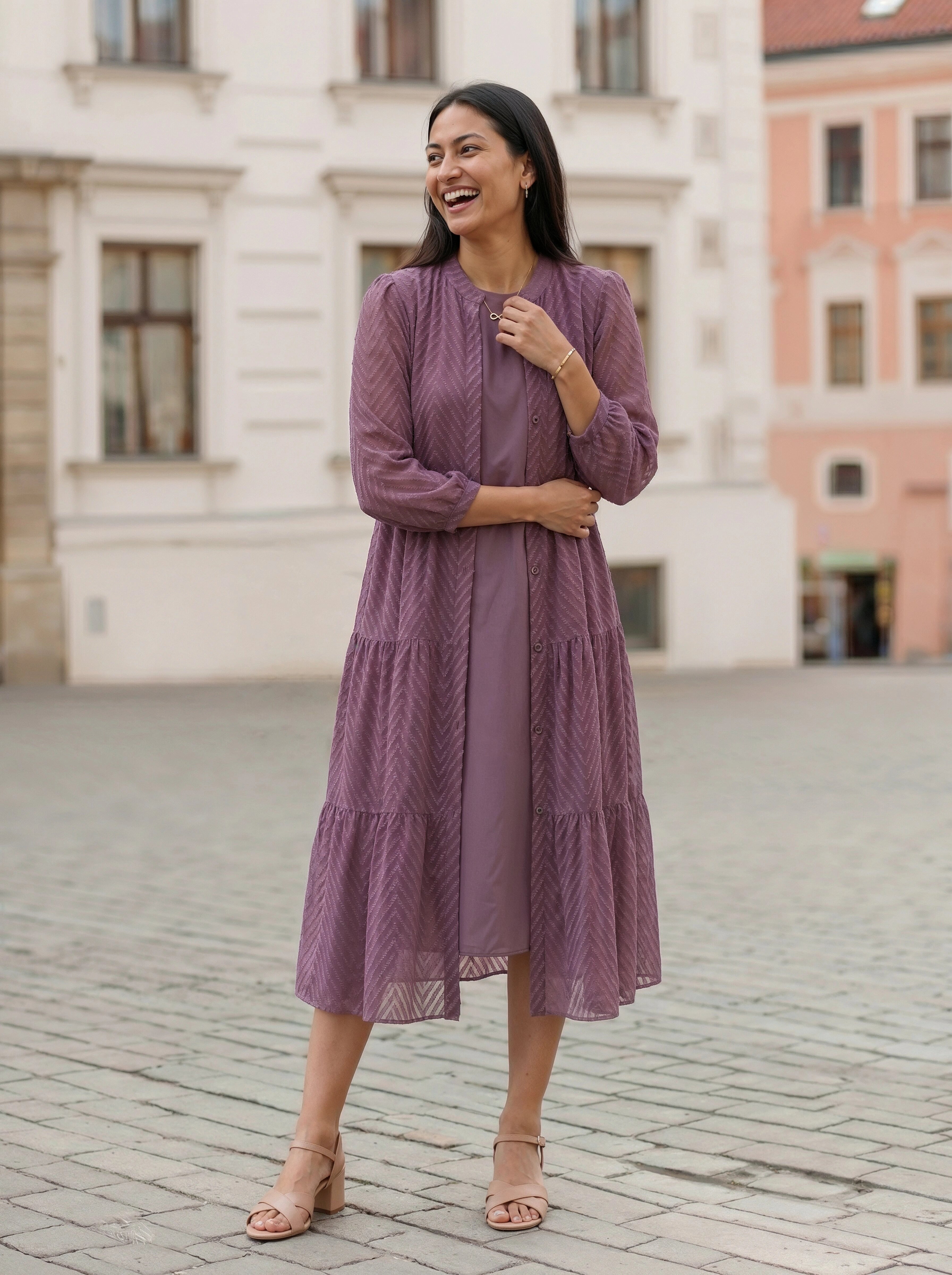 Woman in a purple dress standing on a cobblestone street with buildings in the background