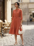 Woman in a rust-colored dress standing on a cobblestone street with outdoor seating in the background.