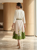 Woman in a white and green dress walking in an indoor setting with wooden walls.