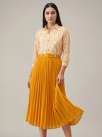Woman wearing a yellow floral shirt and pleated skirt on a plain background