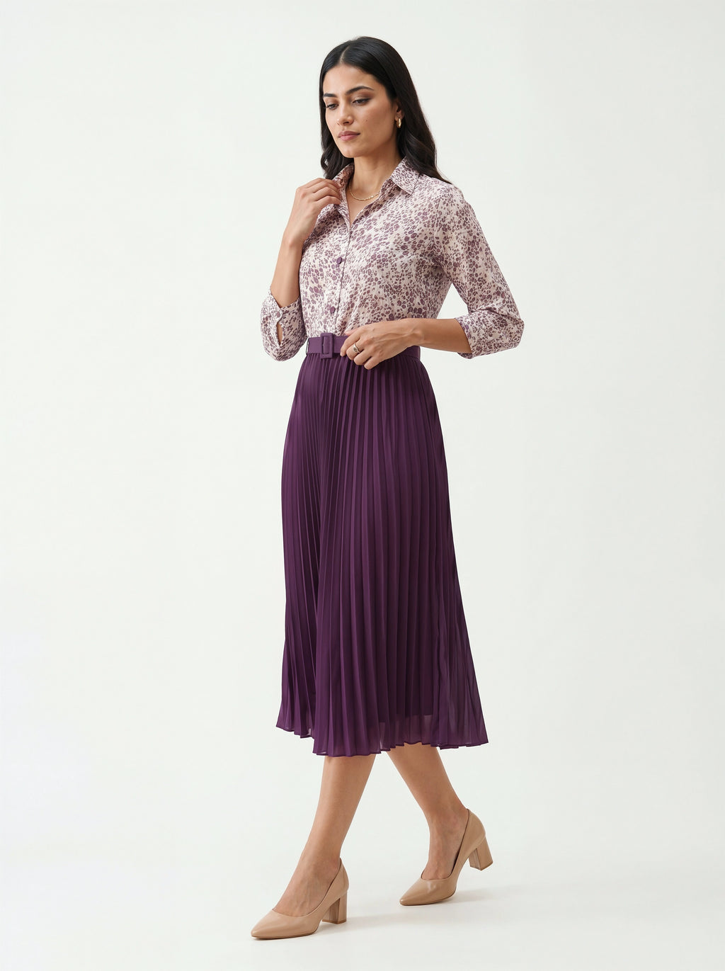 Woman wearing a patterned blouse and purple pleated skirt on a white background