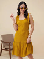 Woman wearing a mustard yellow dress with sunglasses against a beige background