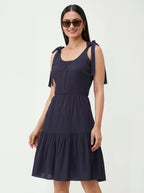 Woman wearing a navy blue dress with bow straps on a white background