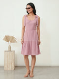 Woman wearing a pink dress standing next to a wooden pedestal with decorative elements.