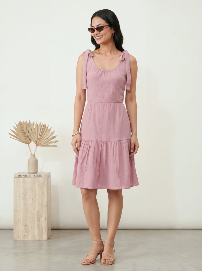 Woman wearing a pink dress standing next to a wooden pedestal with decorative elements.
