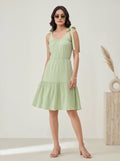 Woman wearing a light green dress with ribbon straps against a plain background
