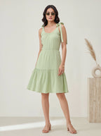 Woman wearing a light green dress with ribbon straps against a plain background