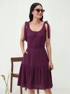 Woman wearing a purple dress with ruffled straps against a white background