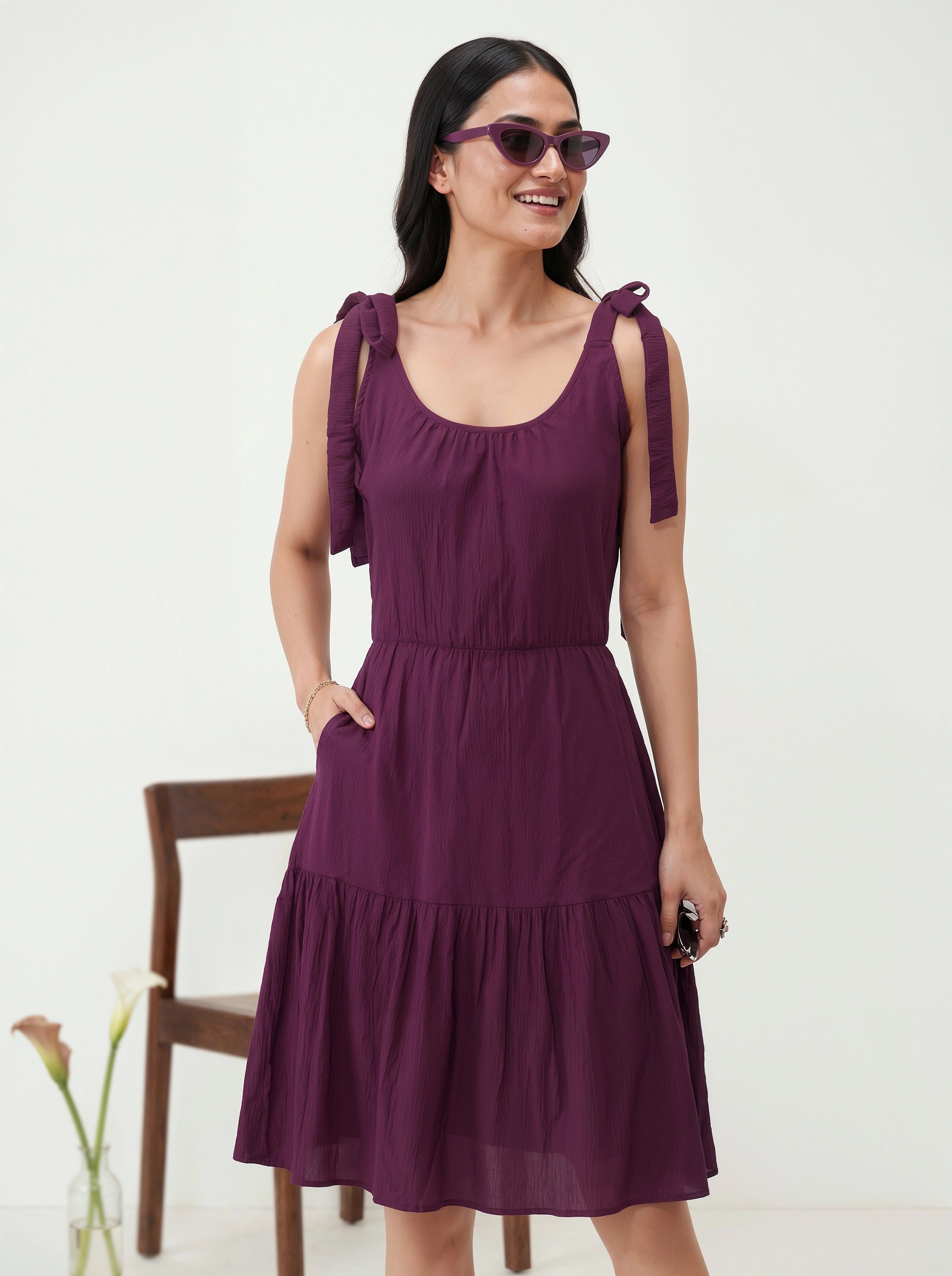 Woman wearing a purple dress with ruffled straps against a white background