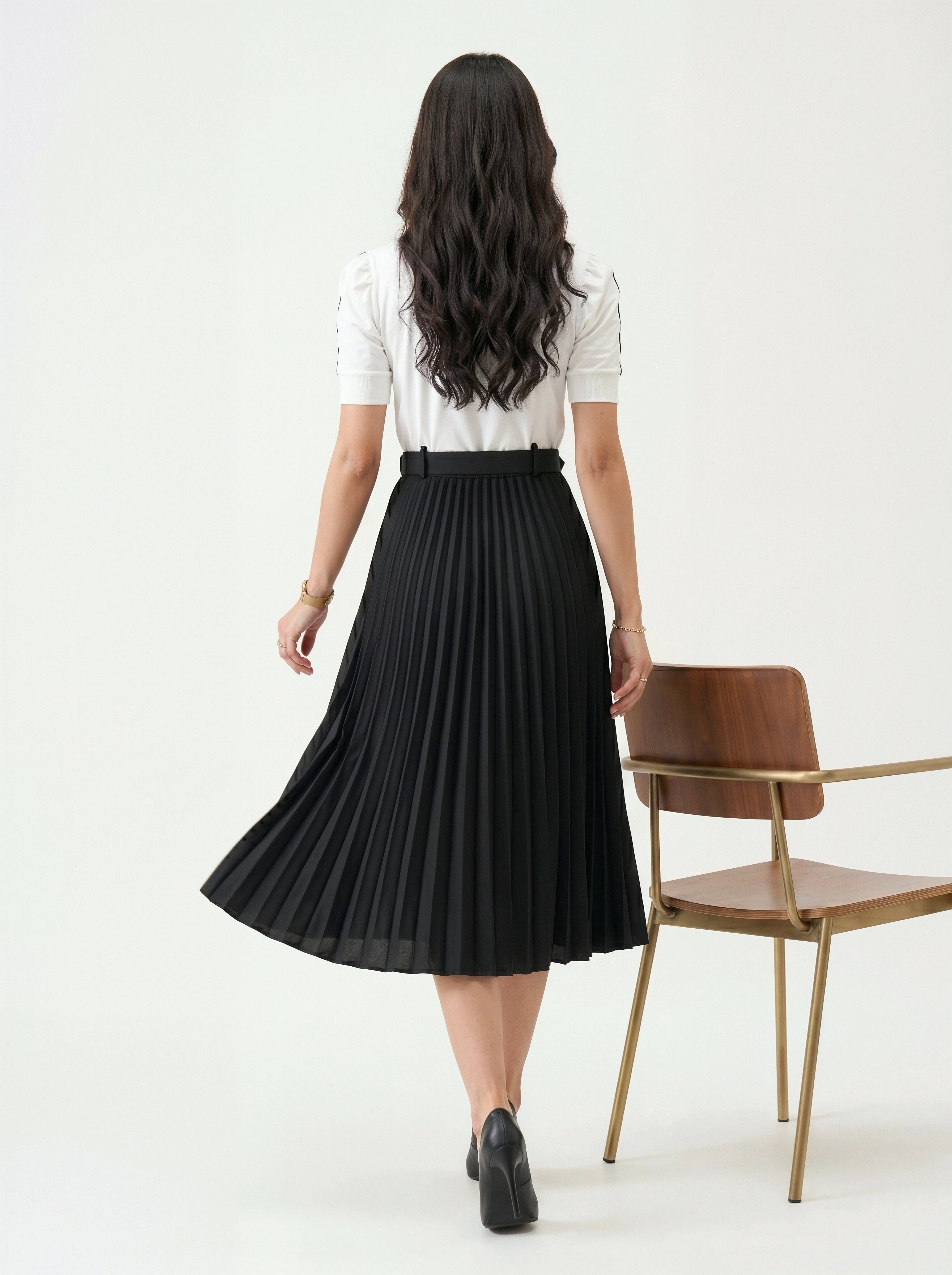Woman wearing a black pleated skirt and white top on a white background