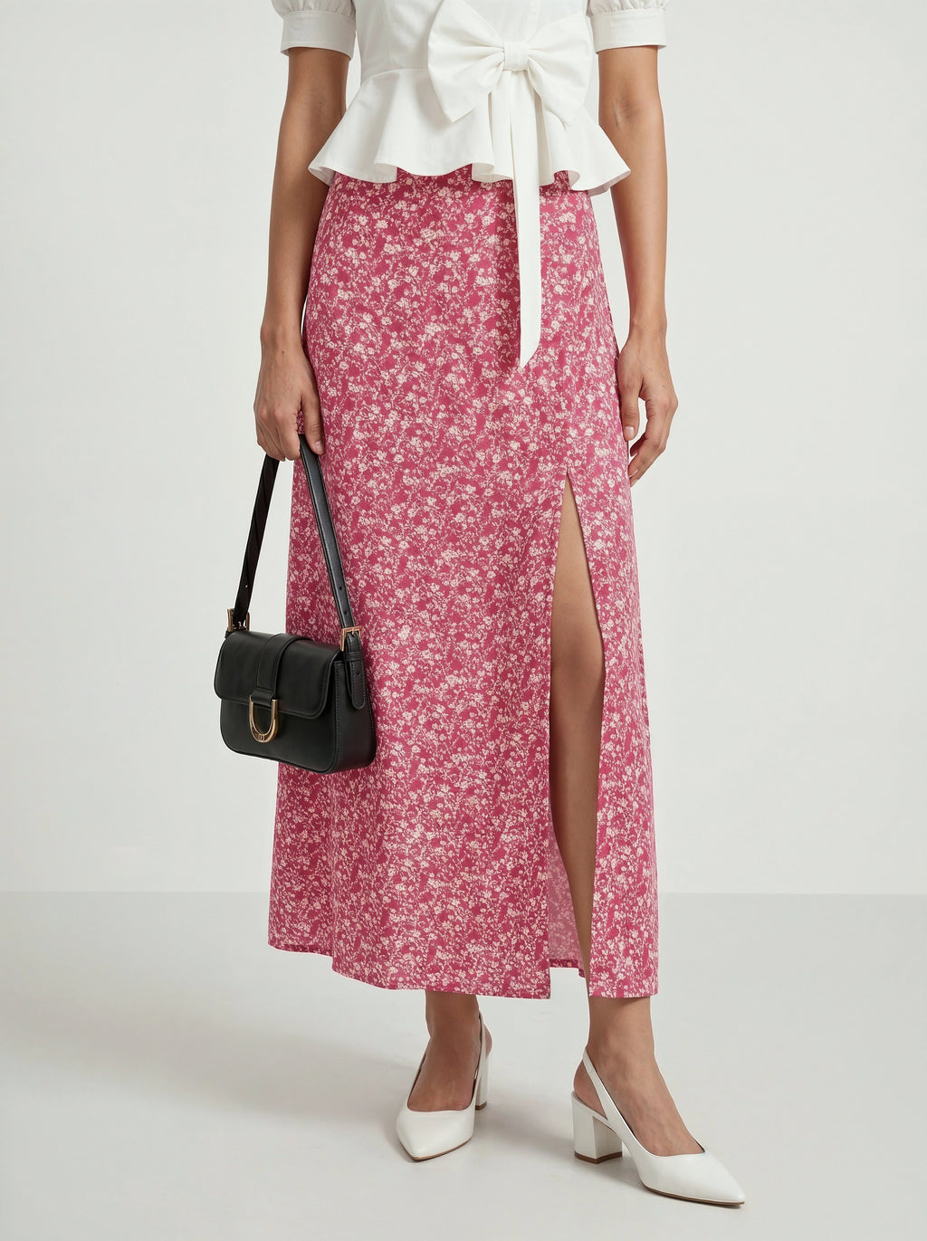 Woman wearing a white blouse and pink floral skirt with a black handbag on a white background