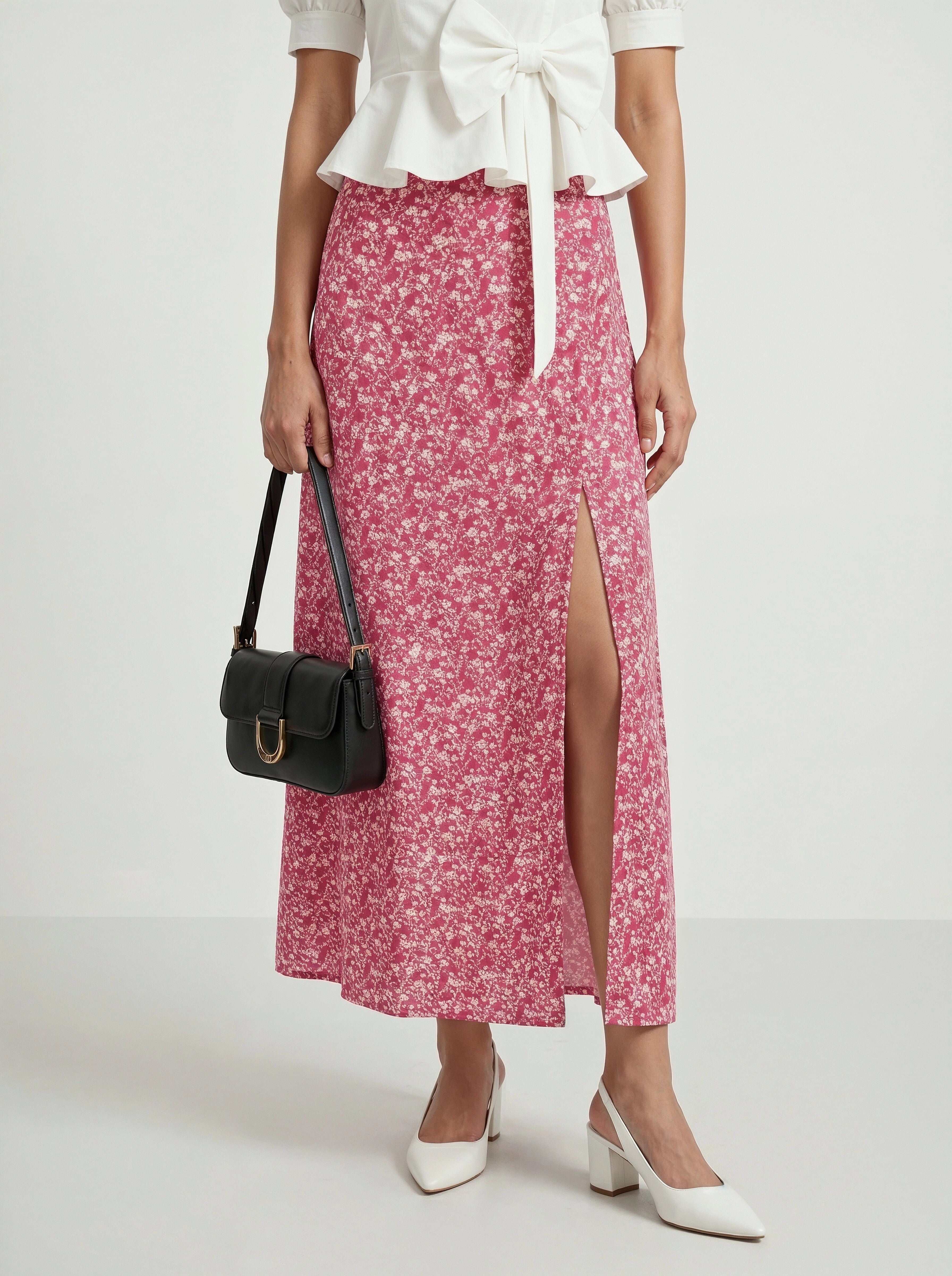 Woman wearing a white blouse and pink floral skirt with a black handbag on a white background