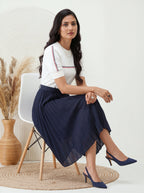 Woman sitting on a chair wearing a white top with red and blue accents and a navy skirt.