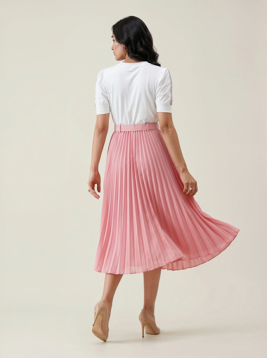Woman wearing a white top and pink pleated skirt on a plain background