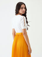Woman wearing a white top with orange accents and a yellow pleated skirt on a white background