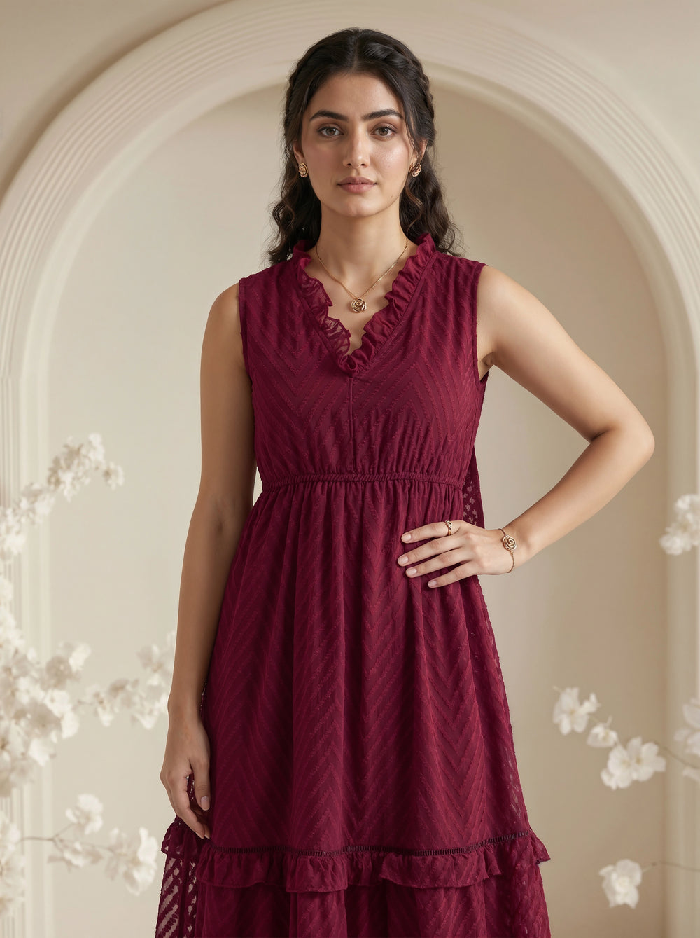 Woman wearing a burgundy dress with floral decorations in a softly lit room.