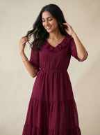 Woman wearing a burgundy dress with ruffled details against a beige background