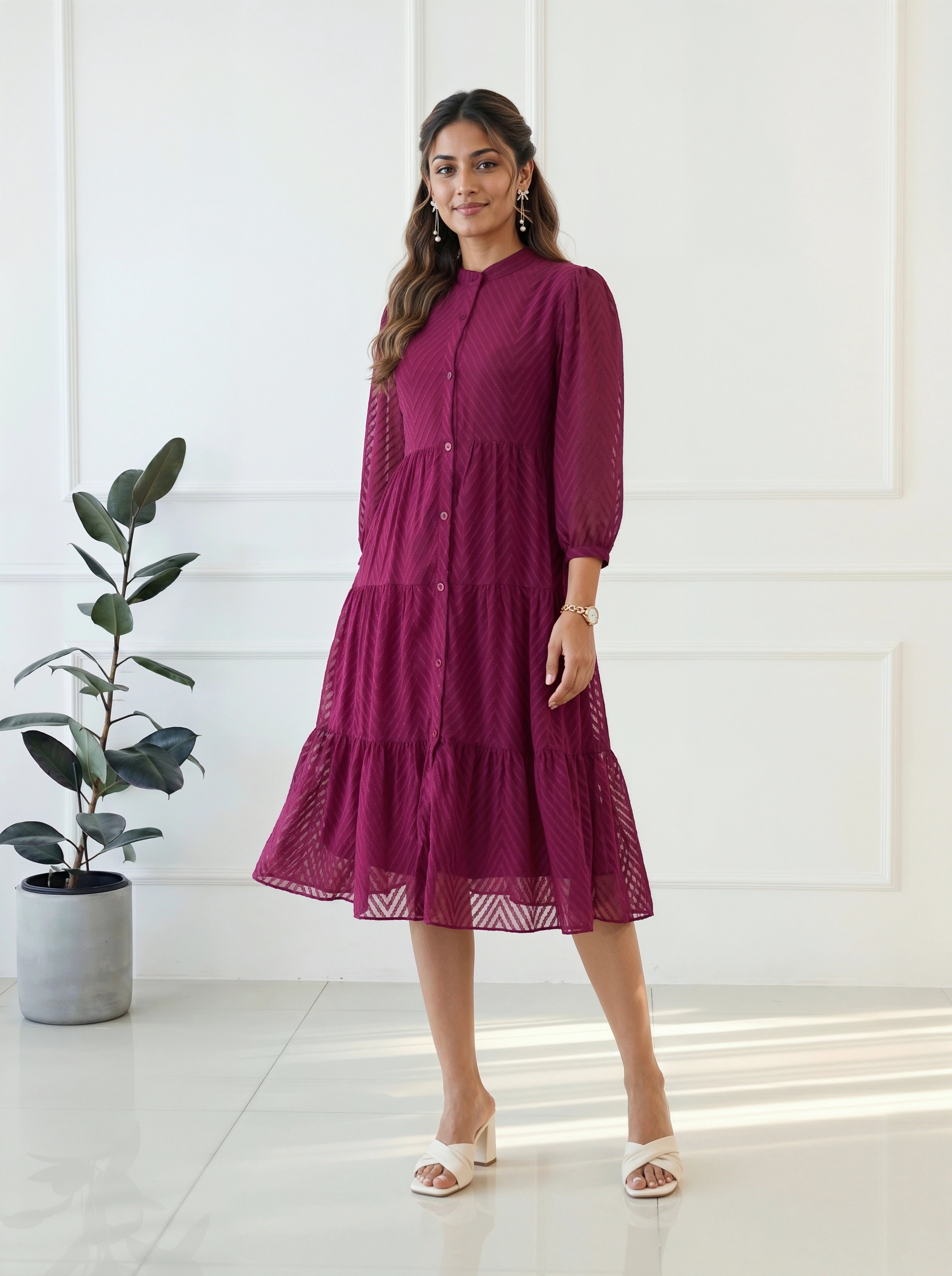 Woman wearing a burgundy dress standing in a bright room with a plant in the background