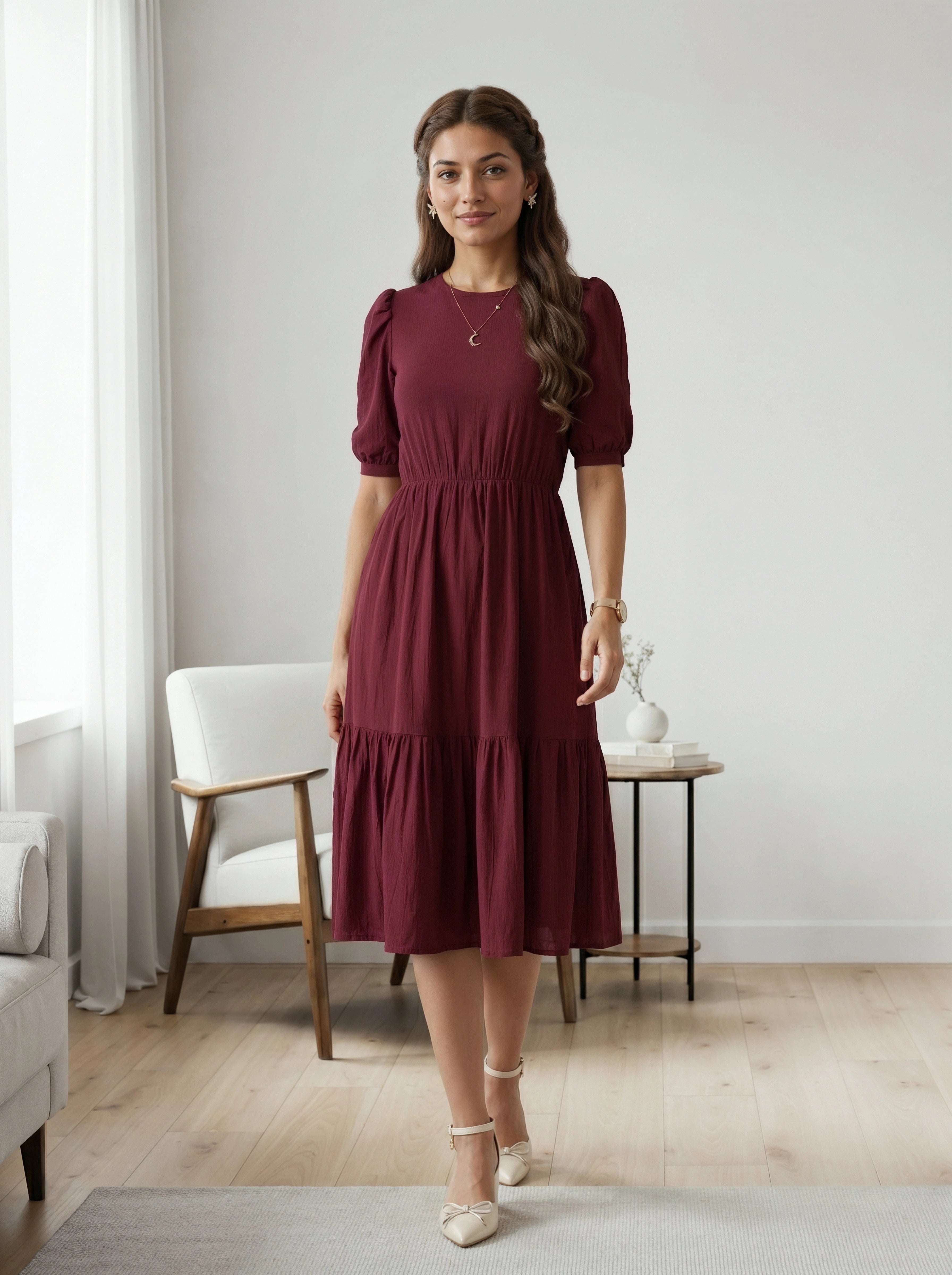 Woman wearing a burgundy dress standing in a room with a white chair and table.