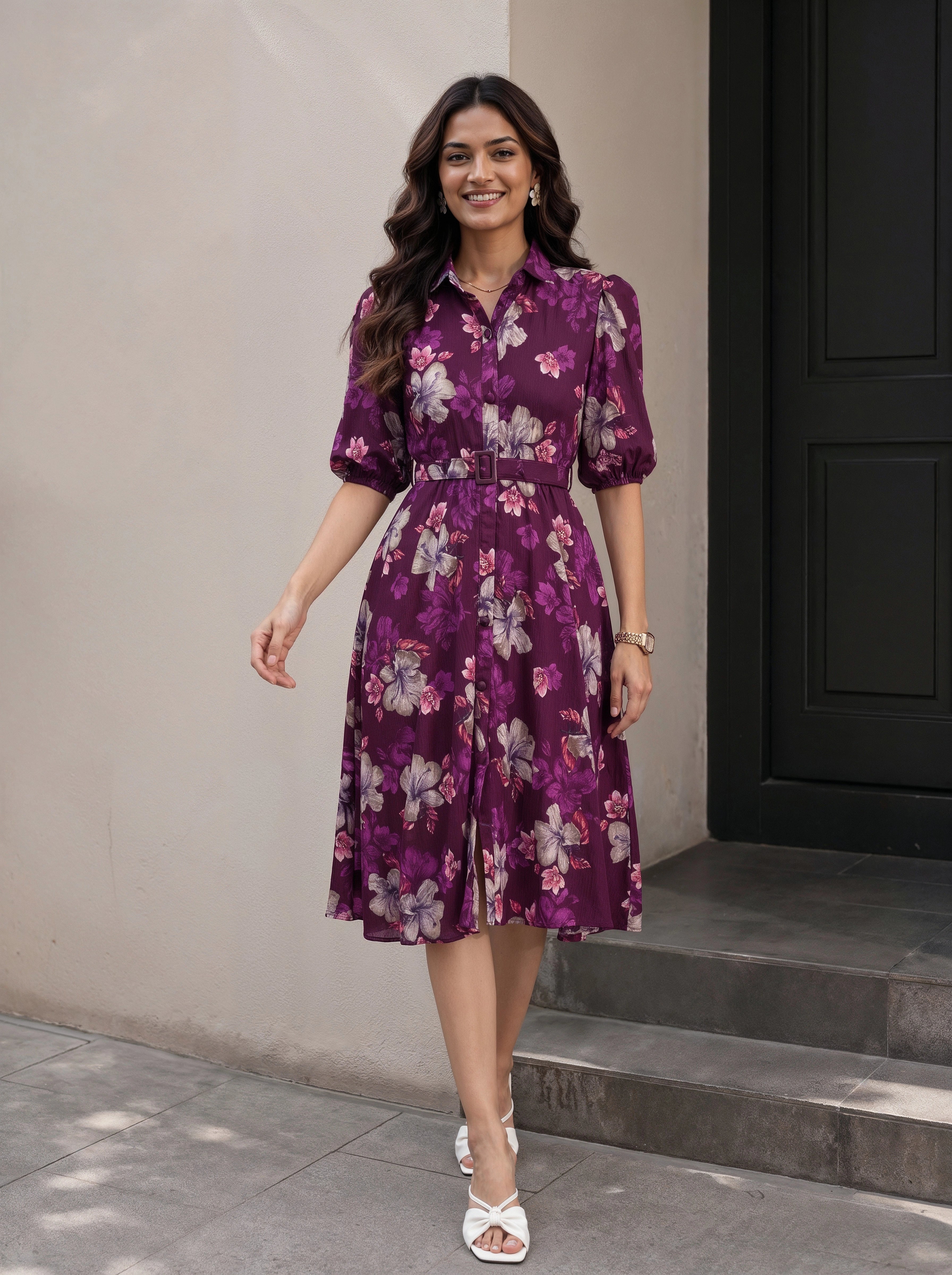 A woman models a black midi dress with three-quarter sleeves, a keyhole tie neckline, side pockets, and a tiered skirt. She is standing in a minimalist studio setting with a beige background, a small wooden stool, and a white vase.