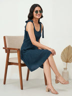 Woman in a blue dress sitting on a wooden chair with a neutral background