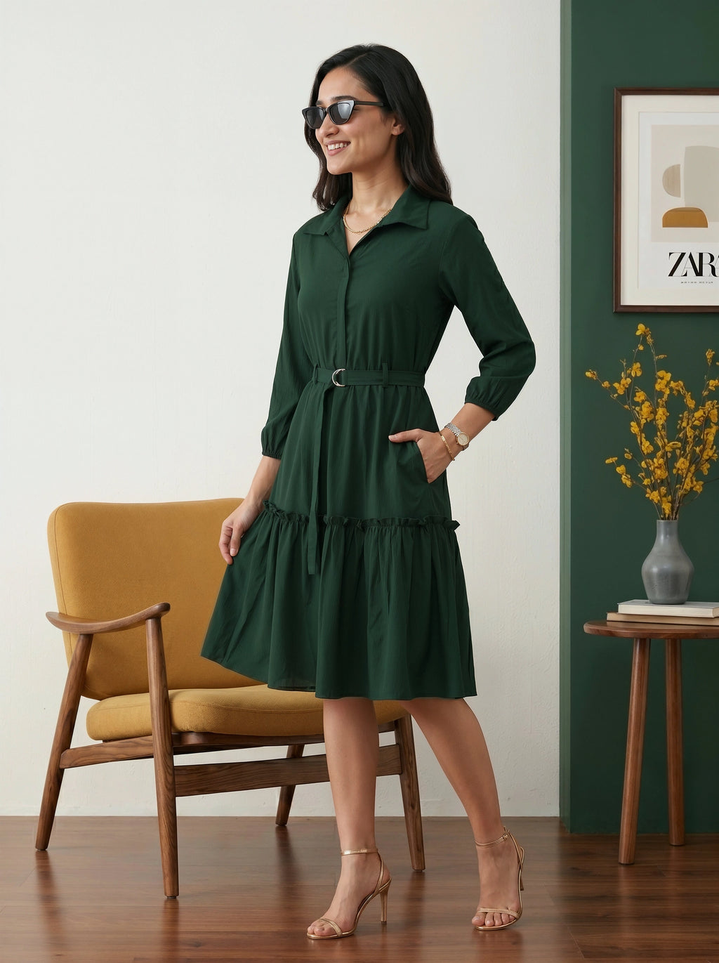 Woman in a green dress standing in a room with a yellow chair and a vase of flowers.